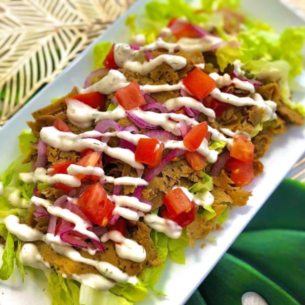 Vegan doner kebab with lettuce, tomatoes, red onions, and white sauce on a rectangular plate.