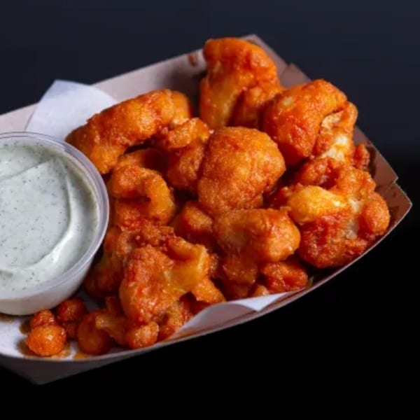 Vegan buffalo cauliflower bites with a side of creamy green dipping sauce in a paper tray.