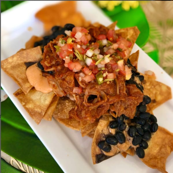 Vegan nachos with black beans, pulled jackfruit, salsa, and a creamy orange sauce.