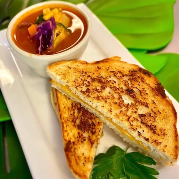 Vegan grilled cheese sandwich with a side of colorful vegetable soup on a white plate.