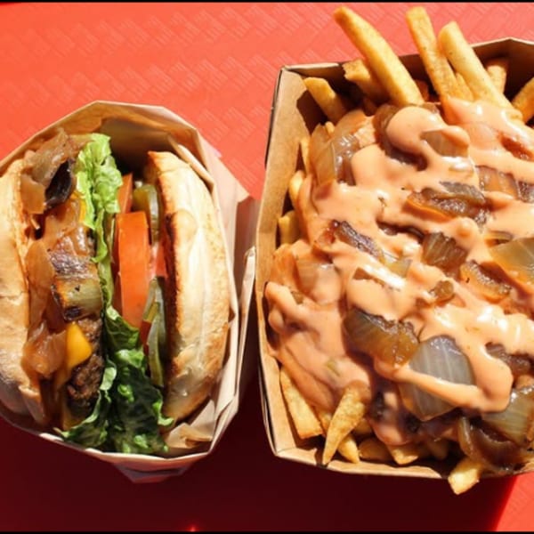 A vegan burger with lettuce, tomato, and caramelized onions next to fries with sauce and onions.