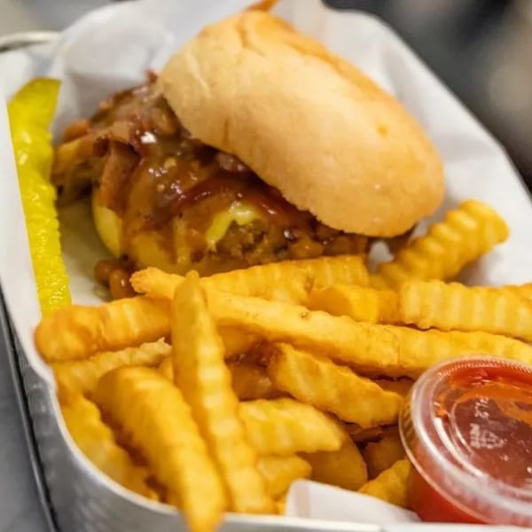 Vegan cheesesteak with crinkle-cut fries, a pickle spear, and ketchup in a white basket.