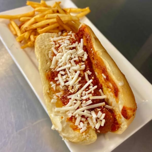 Vegan meatball sub with marinara sauce and shredded cheese, served with a side of fries.