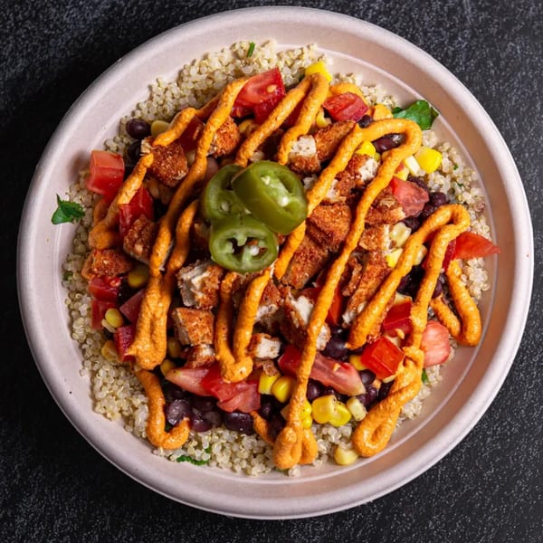 Overhead view of a vegan quinoa bowl with plant-based chicken, corn, black beans, tomatoes, and jalapeños.