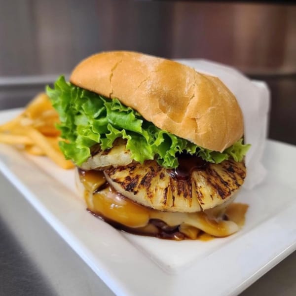 A vegan burger with grilled pineapple, lettuce, and sauce, served with fries on a white plate.