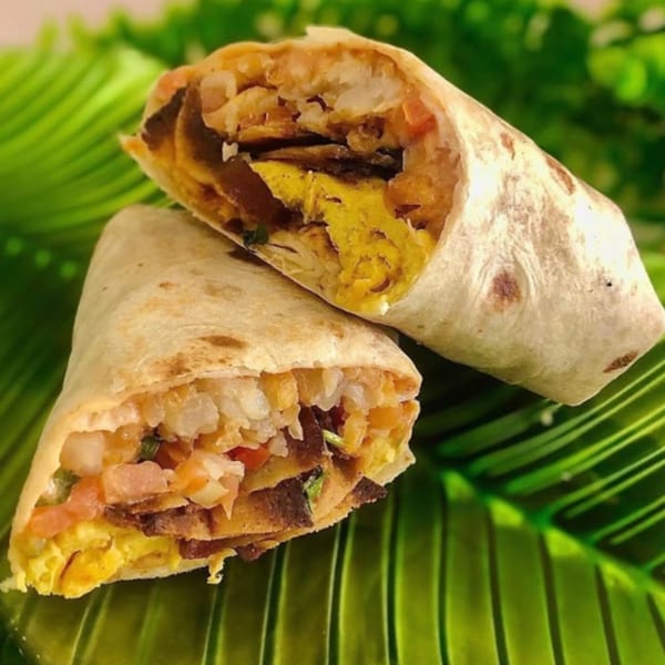 Two vegan breakfast burritos, cut in half, revealing scrambled tofu, hash browns, and pico de gallo.